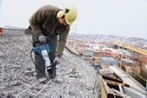 安全装備を身に着けた人が解体用ハンマーを使って屋上のコンクリートを破壊しています。