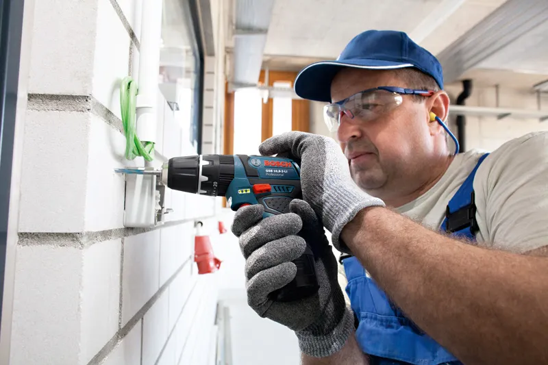 安全装置を装着した人が壁でコードレスコンビドリルを使用しています。.