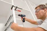 安全装置を装着した人がコードレスドリルを使用してキャビネットを組み立てています。.
