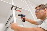 安全装置を装着した人がコードレスドリルを使用してキャビネットを組み立てています。.