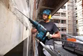 安全装備を身に着けた人が、建設現場で解体用ハンマーを使ってコンクリートを破壊しています。