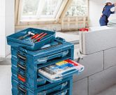 積み重ねられた工具箱と、さまざまな留め具が入った開いた引き出し。背景には安全装備を身に着けた人物がいます。