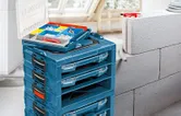 積み重ねられた青い工具箱と、近くにネジや壁のプラグが入った開いた整理トレイ。