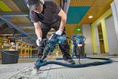 安全装備を身に着けた人が解体用ハンマーを操作してタイル張りの床を壊しています。