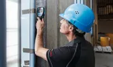 安全装備を身に着けた人が、ウォールスキャナー検出器でコンクリートの壁をスキャンします。