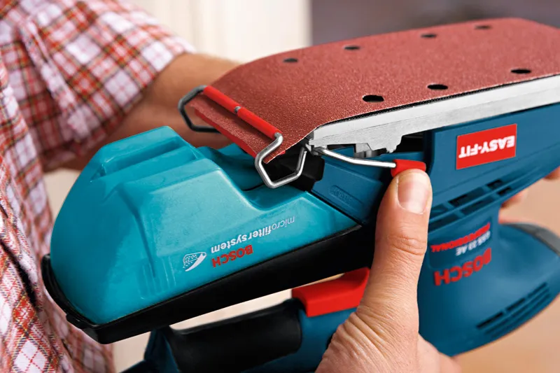 人がオービタルサンダーにサンドペーパーを取り付けています。