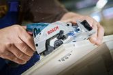 コードレス丸鋸を使用して木の板を切る人。