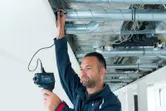 天井の HVAC パイプを検査するために温度検出器を使用している人。