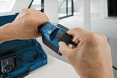 開いたケースの横にある電動工具のバッテリーに充電ケーブルを接続する人。.