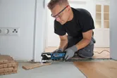安全装備を身に着けた人が、出入り口の近くでマルチカッターを使用して床板をトリミングしています。.