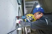 安全装備を身に着けた人が回転ハンマーでコンクリートに穴を開けています。