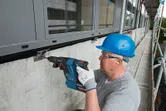 安全装備を身に着けた人が建設現場でコンクリートの壁に穴を開けています。