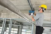 安全装備を身に着けた人が建設現場で天井に穴を開けている。.
