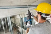 建設工事中に、安全装備を身に着けた人がコンクリートの天井に穴を開けています。