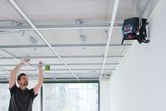 レーザーレベルツールを取り付けた吊り天井フレームの上で水準器を使用している人。