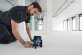 レーザーレベルツールとアクセサリを使用して、建設現場の床に線を引いている人。