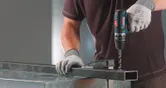 安全装置を装着した人が、FlexiClick アダプターを使用して金属梁に穴を開けます。