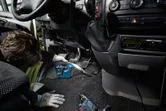 安全装備を身に着けた人がコードレス掃除機で車の床を掃除しています。