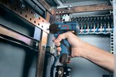 コードレスインパクトレンチを使用して、電気パネル内のボルトを締めます。.