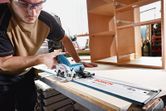 安全装置を装着した人が作業場でコードレス丸鋸を使用して木材を切断しています。