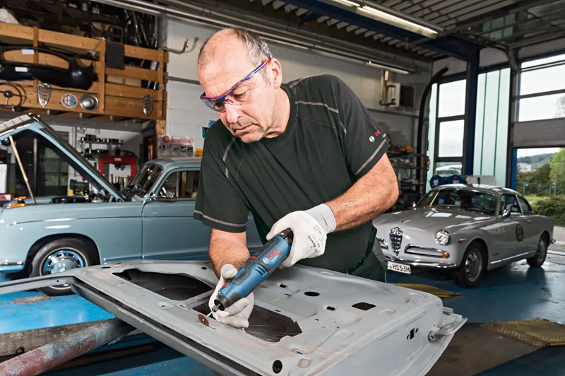 安全装置を装着した人がガレージでコードレス回転工具を使って金属を研磨しています。.