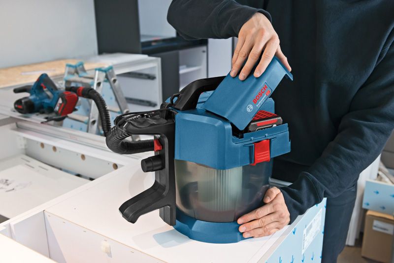 作業台の上でコードレス集塵機にバッテリーを挿入する人。.