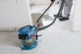 コードレス集塵機を使用してコンクリートの床から液体を除去している人。
