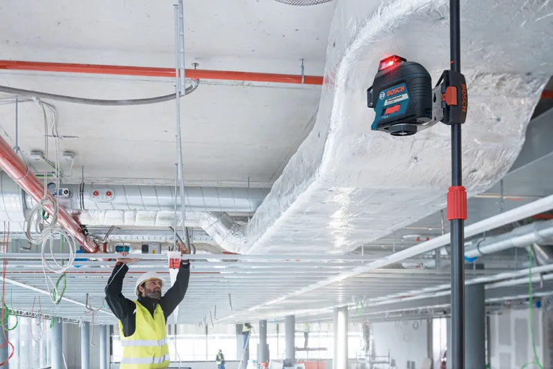 安全装置を装着した人がレーザーレベル測定ツールを使用して天井フレームの位置を調整します。.