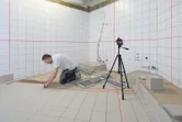 三脚に取り付けたレーザーレベル測定ツールを使用して浴室にタイルを設置している人。