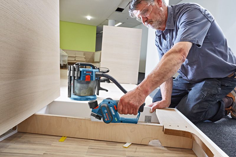 安全装置を装着した人がコードレスかんなを使用して木製パネルを滑らかにしています。.