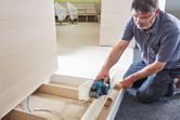 コードレスプレーナーを使用して、現場の床にある木の板を滑らかにしている人物。
