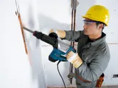 安全装備を身に着けた人が解体用ハンマーを使用して壁に溝を壊しています。