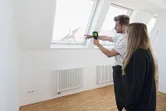 明るい部屋の窓の近くで、ある人が別の人にサーモカメラの使い方を説明しています。