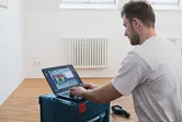 ラジエーターのある部屋でノートパソコンを使ってサーマルカメラのデータを分析している人。