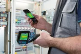 サーモカメラとスマートフォンを使用して、電気パネルの熱パターンを確認している人。
