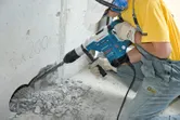 安全装備を身に着けた人が回転ハンマーでコンクリートに穴を開けています。.