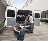 オープンバンの近くにいる 2 人の作業員が工具を整理し、コードレス掃除機を使用しています。.