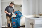 改装中のキッチンで、ドリルの入った青い工具収納ボックスを開ける人。
