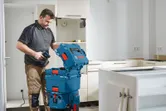 改装中のキッチンで、ドリルの入った青い工具収納ボックスを開ける人。