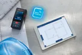 建物の設計図の横にレーザー距離計が置かれ、タブレットにはデジタルフロアレイアウトが表示されています。