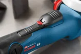 質感のある黒いグリップと赤い安全スイッチを備えた電動工具のハンドルのクローズアップ。