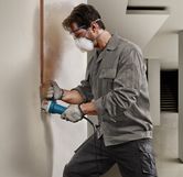 安全装置を装着した人が電動工具を使用して壁に垂直の溝を切っています。
