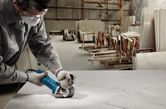 安全装置を装着した人が作業場でアングルグラインダーを使ってスラブを切断しています。