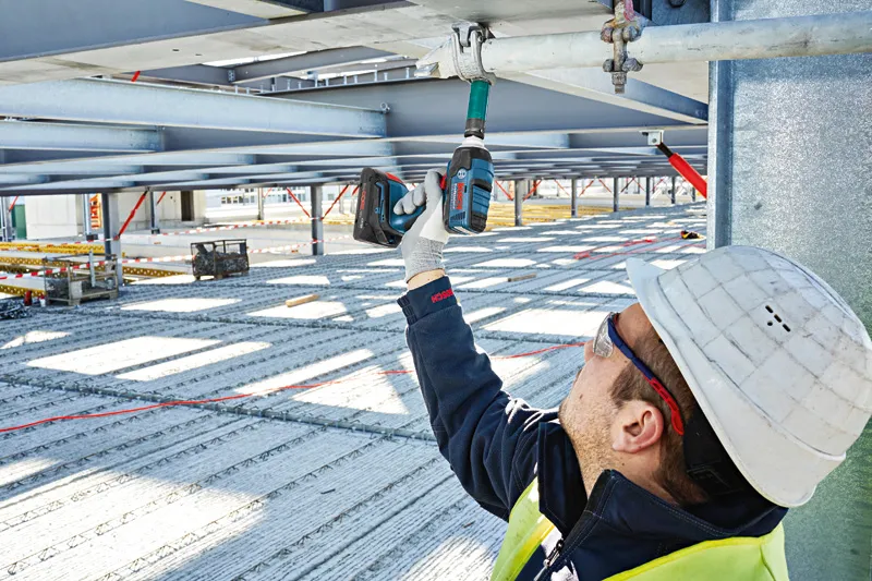 安全装置を装着した人が金属梁に対してコードレスインパクトレンチを使用しています。.