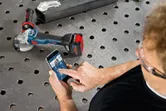 金属製の作業台でスマートフォンのアプリを使用してコードレスアングルグラインダーを操作する人。
