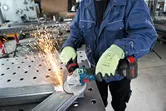 安全装備を身に着けた人が作業場で金属を研磨し、火花を散らしています。