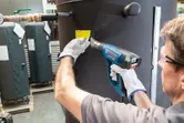 安全装備を身に着けた人がヒートガンを使用して大きな金属製のタンクにラベルを貼っています。