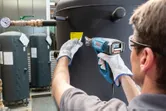安全装備を身に着けた人がヒートガンを使用して大きなタンクにラベルを貼っています。