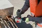 安全装備を着けた人がアングルグラインダーで鉄筋を切断し、火花が出ています。