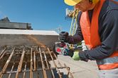 安全装備を身に着けた人が、建設現場でアングルグラインダーを使用して錆びた鉄筋を切断しています。